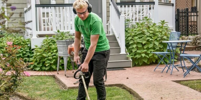 man in green t-shirt and black pants holding black and brown weed eater FEATURED IMAGE