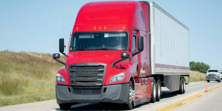 a red semi-truck driving down a highway FEATURED IMAGE
