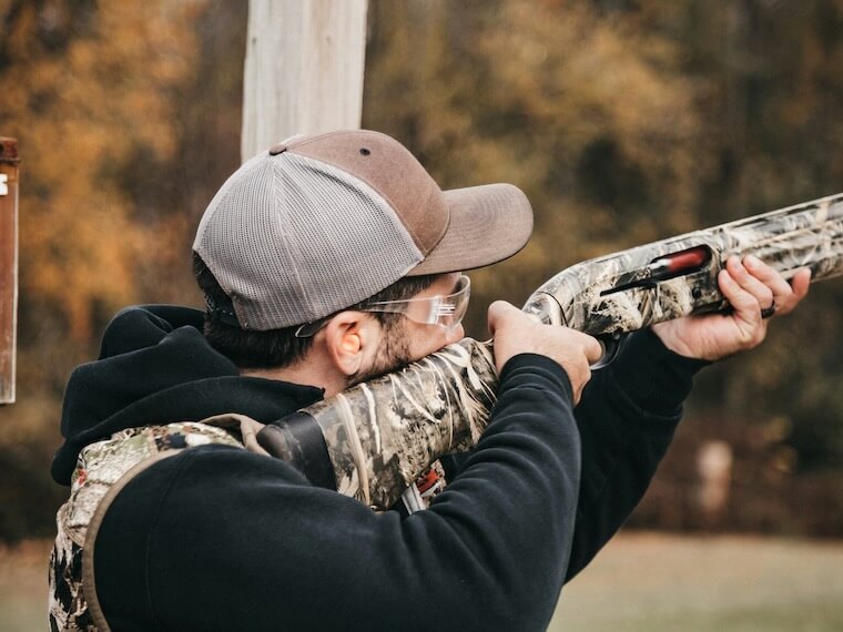 a man with a hat and glasses aims a rifle