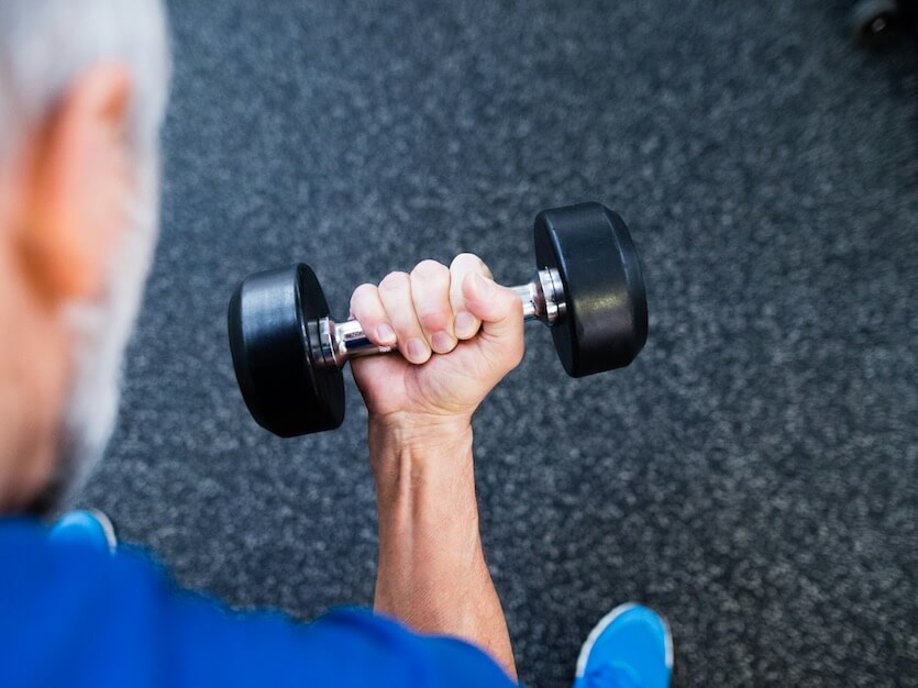 unrecognizable senior man in sports clothing in gym working out with weights