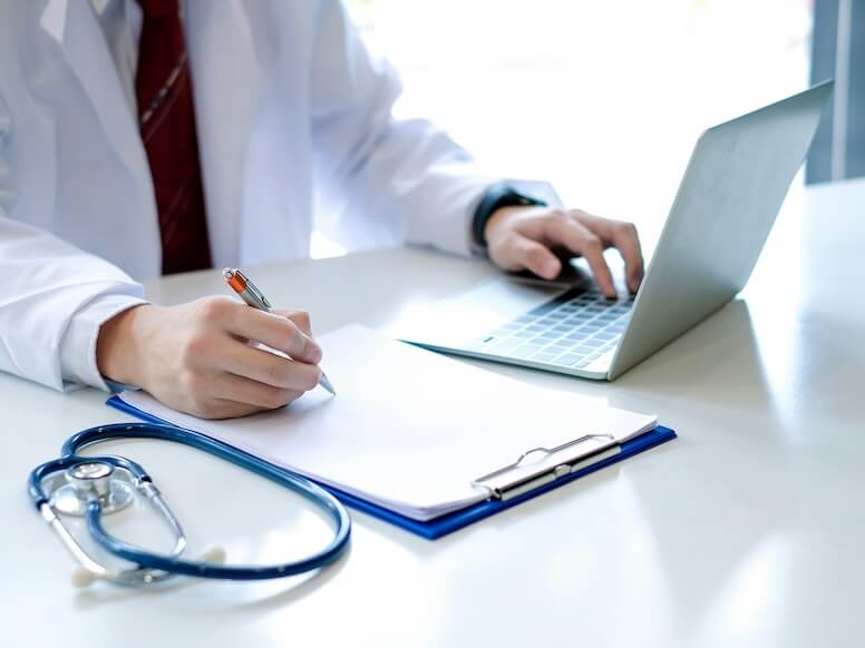 doctor working a billing document on a laptop at hospital