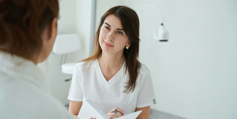 gynecologist talking with female patient during medical consultation and writing her new symptoms in notebook in modern clinic FEATURED IMAGE