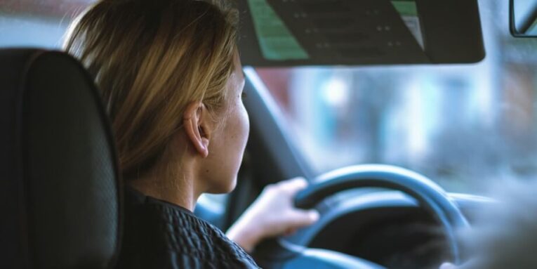 a woman sitting in a car with a steering wheel FEATURE IMAGE