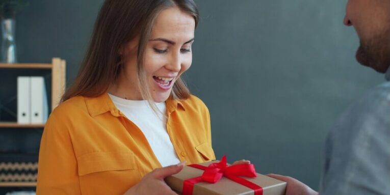 man gives woman a wrapped gift with red ribbon FEATURED IMAGE