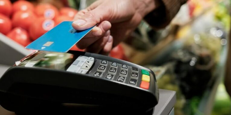 a person holding a credit card in front of a cash register FEATURED IMAGE