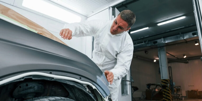 covering car by brown cloth caucasian automobile repairman in uniform works in garage FEATURED IMAGE