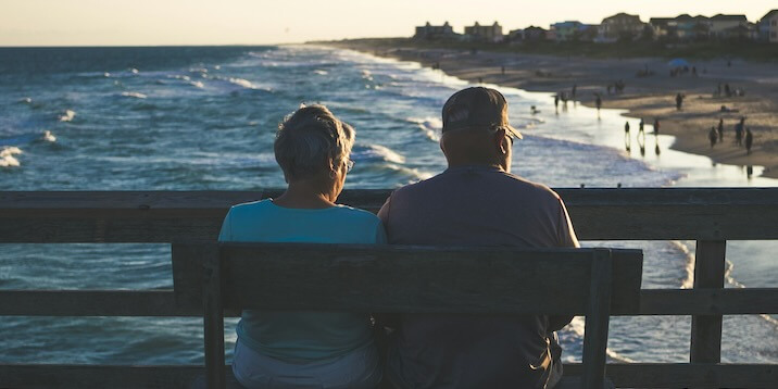 man and woman sitting on bench in front of beach FEATURE IMAGE