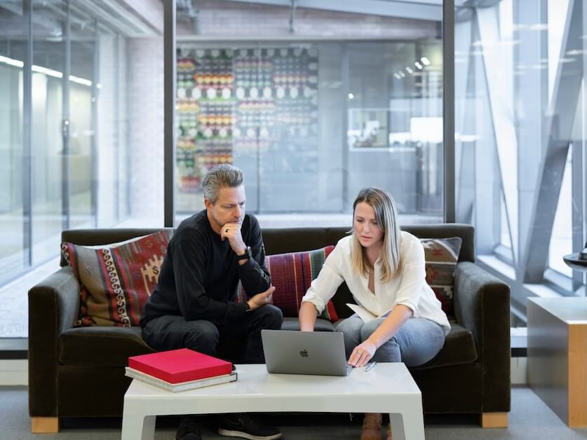 man and woman sitting on couch using macbook
