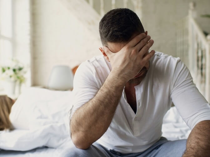 man sitting on bed with hand over face