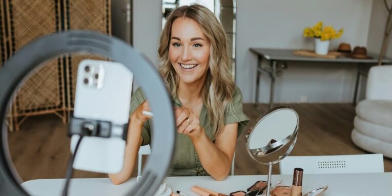 a woman sitting at a table in front of a mirror getting ready to record a video - FEATURED IMAGE