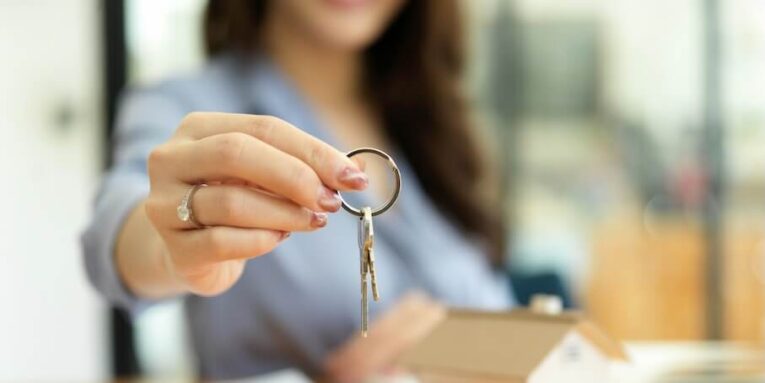 female residential broker real estate agent holding house keys in hand property investment concept FEATURED IMAGE