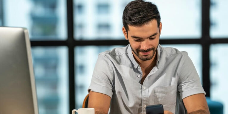 portrait of smiling caucasian man in office worker using smartphone with internet in modern office FEATURED IMAGE