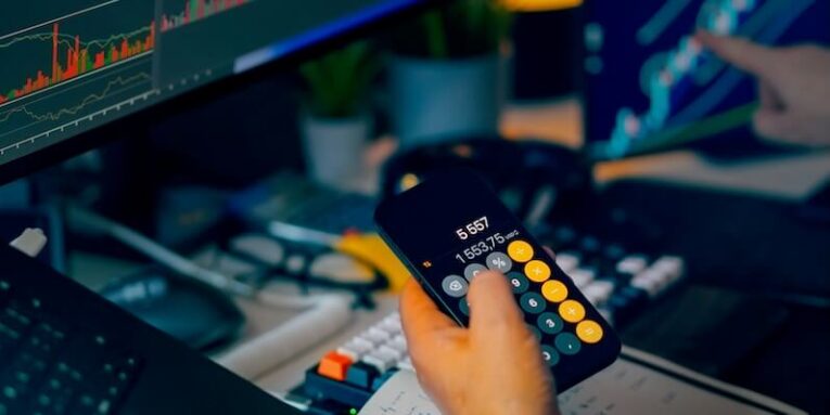 trader analyzing stock market charts on computer screens with calculator