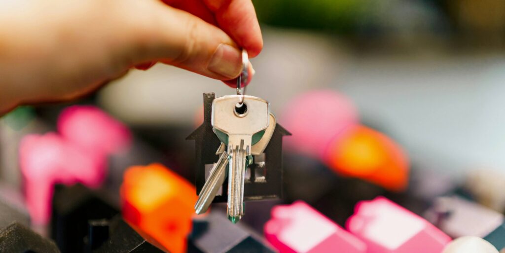 hand holding house keys over miniature houses Featured Image