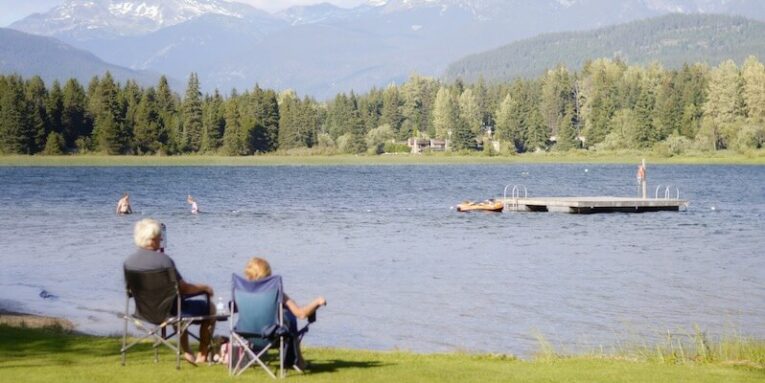 two persons sitting on grass facing the lake FEATURED IMAGE