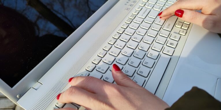 a woman is typing on a laptop outside FEATURED IMAGE