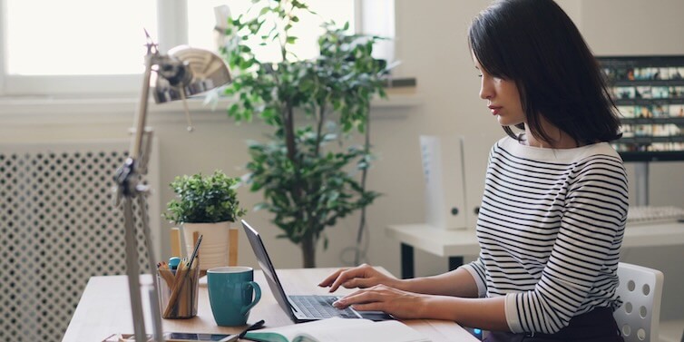 a woman sitting at a desk using a laptop computer FEATURED IMAGE