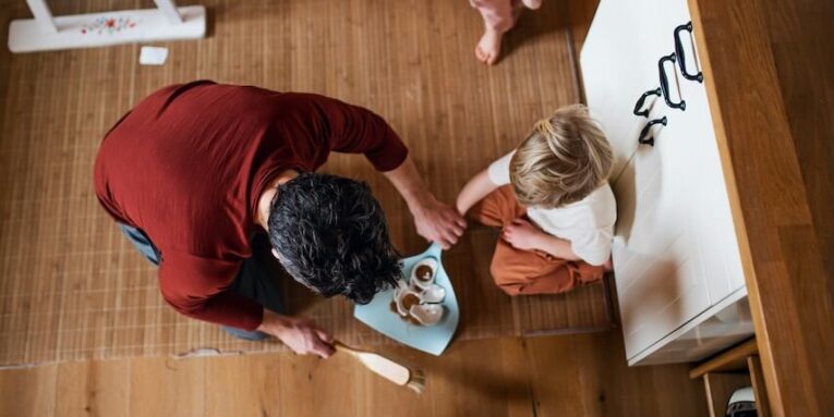 a top view of father with small children sweeping shards at home daily chores concept FEATURED IMAGE