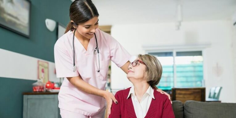 smiling young nurse talking with senior woman sitting on sofa at home FEATURED IMAGE