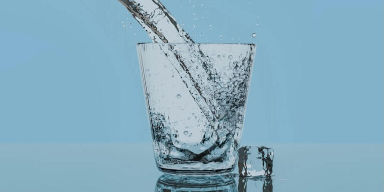 a glass filled with water with a blue background FEATURE IMAGE