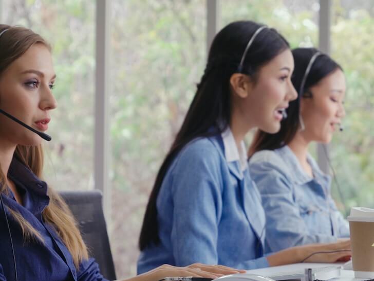customer support agent or call center with headset works on desktop computer while supporting the customer on phone call operator service business representative concept