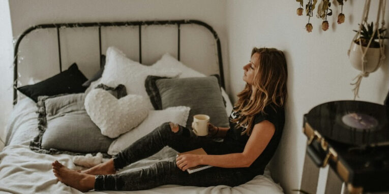 woman leaning on wall while sitting on bed FEATURED IMAGE