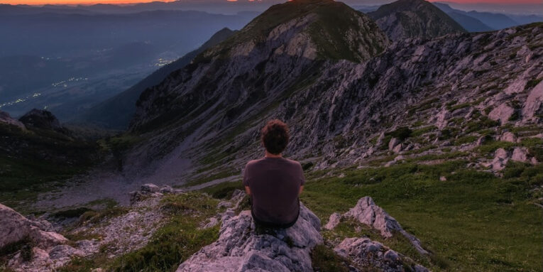 a person sitting on a rock looking at the mountains FEATURED IMAGE