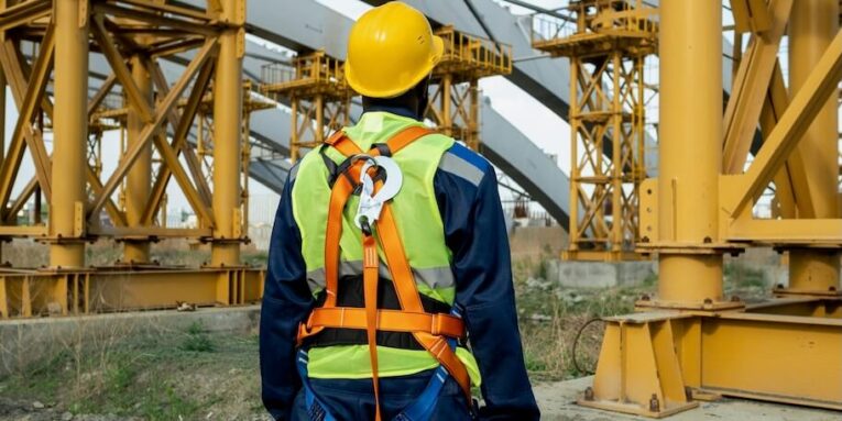 rear view of construction worker in equipment and in work helmet working on construction site FEATURED IMAGE