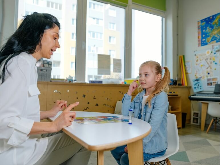 girl on the session of speech therapist lesson on the development of speech in kindergarten teacher spreads out puzzle in front of the child
