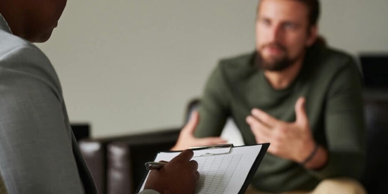 close up of african-american psychotherapist making notes in card during psychotherapy with man FEATURED IMAGE