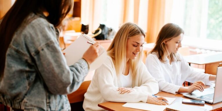 a group of women students sitting at a table working on laptops FEATURED IMAGE