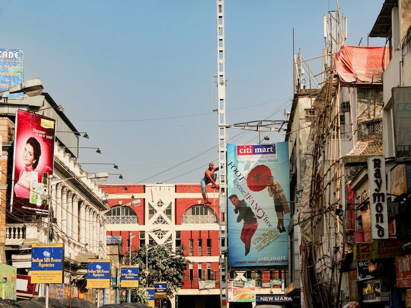 Vibrant daytime street scene in Kolkata featuring billboards and bustling activity.