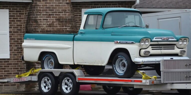 a blue and white truck on a trailer in front of a house FEATURED IMAGE