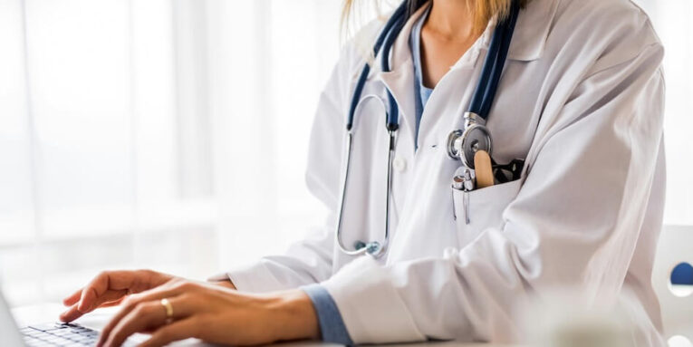 unrecognizable young female doctor working on laptop at the office desk FEATURED IMAGE