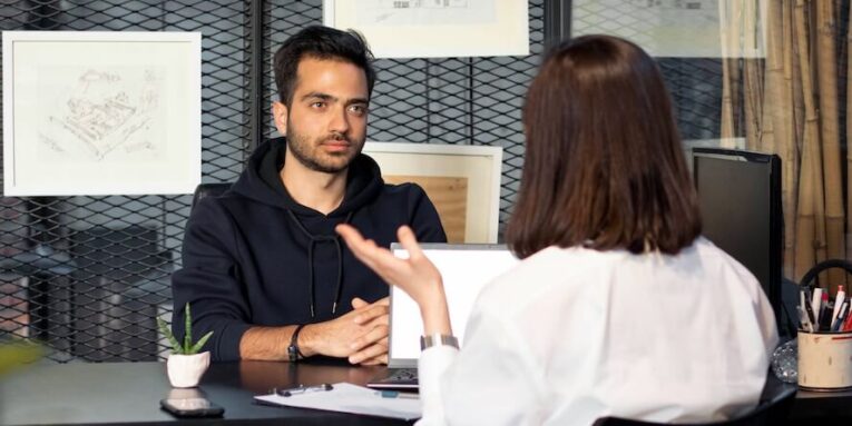 a man sitting at a desk talking to a woman FEATURED IMAGE