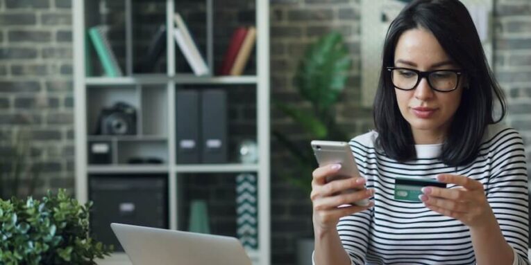 a woman sitting at a table looking at her cell phone FEATURED IMAGE