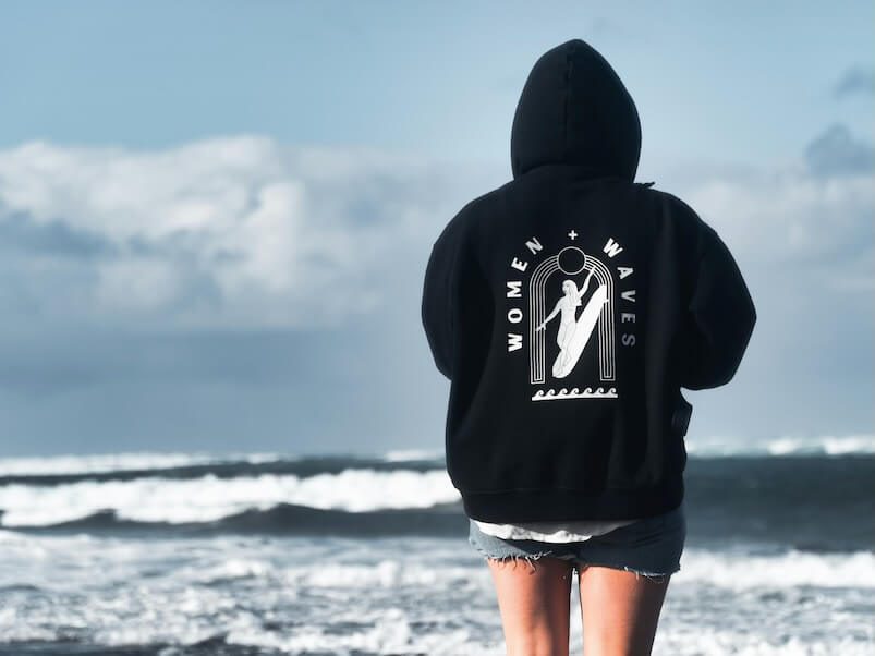 person in black hoodie standing on seashore during daytime