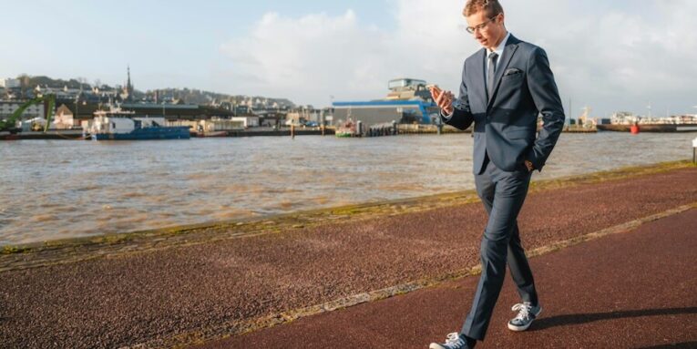 a man standing on a sidewalk near a body of water FEATURED IMAGE