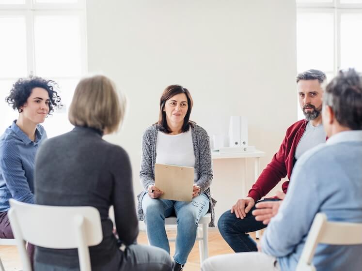 serious men and women sitting in a circle during group therapy talking