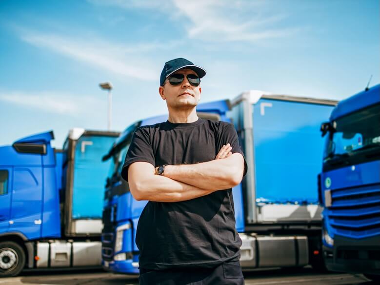 professional truck driver with hat and sunglasses confidently standing in front of big and modern truck bright sunny day people and transportation concept