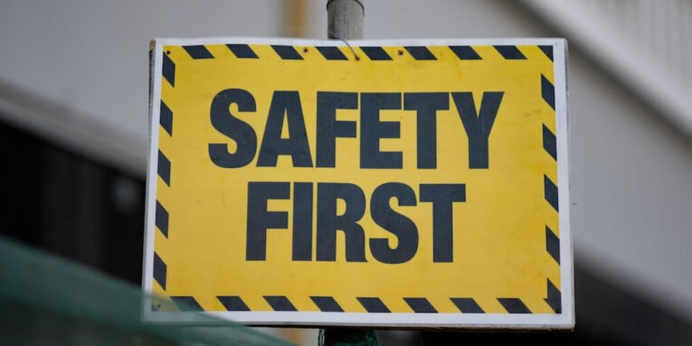 a yellow and black safety first sign on a pole FEATURED IMAGE