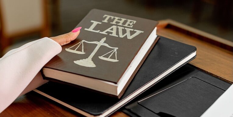 Closeup image of a law book titled 'The Law' on a wooden desk with scales of justice FEATURED IMAGE