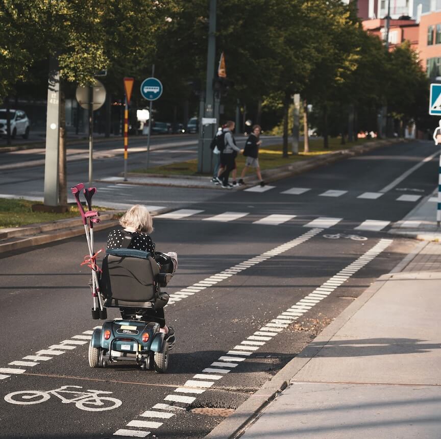 elderly woman in black jacket riding on black and gray scooter on gray asphalt road during daytime