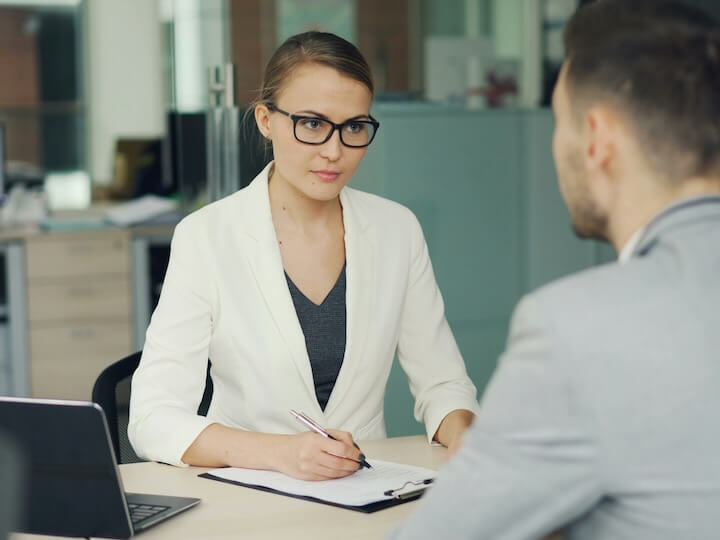 woman in glasses interviews man at office desk