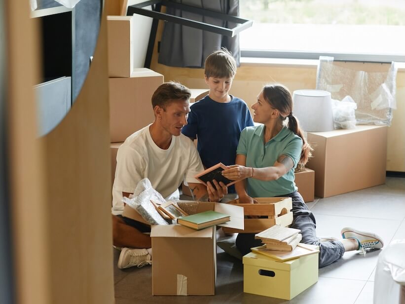 candid portrait of happy family unpacking boxes sitting on floor while moving into new house