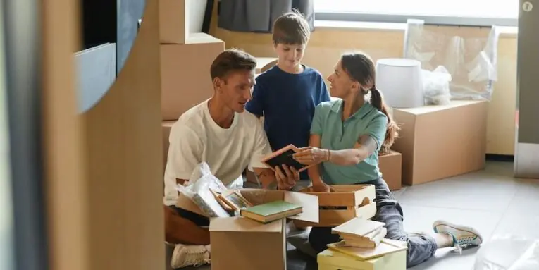 candid portrait of happy family unpacking boxes sitting on floor while moving into new house FEATURED IMAGE