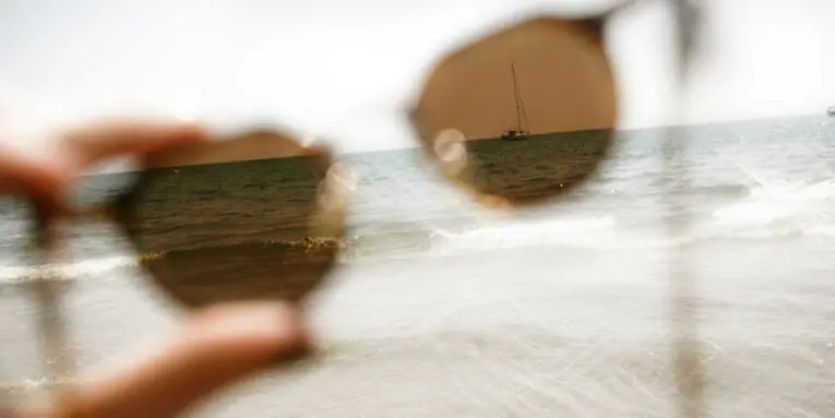 hand holding sunglasses with beach and ocean background FEATURED GUEST