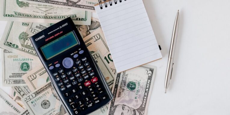 Flat lay of US dollar bills with calculator and notebook for budgeting FEATURED IMAGE