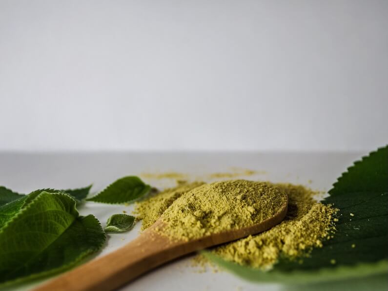 Image showcasing a close-up of herbal powder on a wooden spoon surrounded by green leaves.
