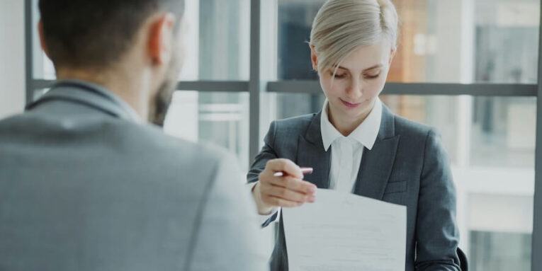 woman in suit shows document to man FEATURED IMAGE